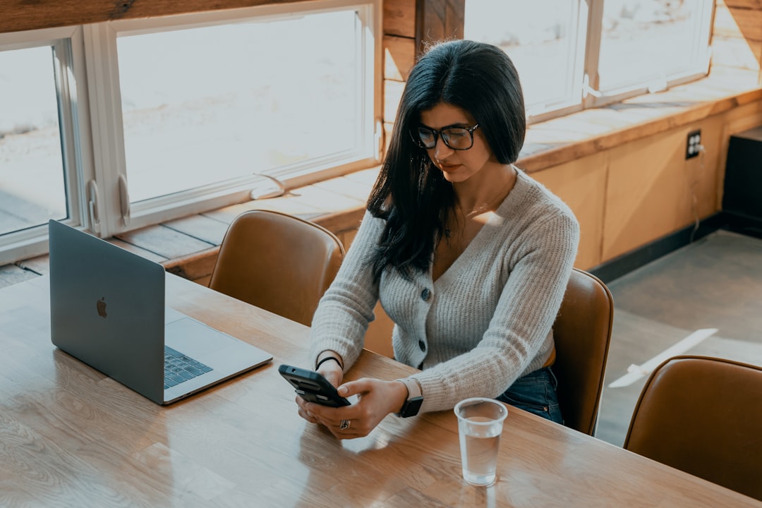 woman in white cardigan holding black smartphone