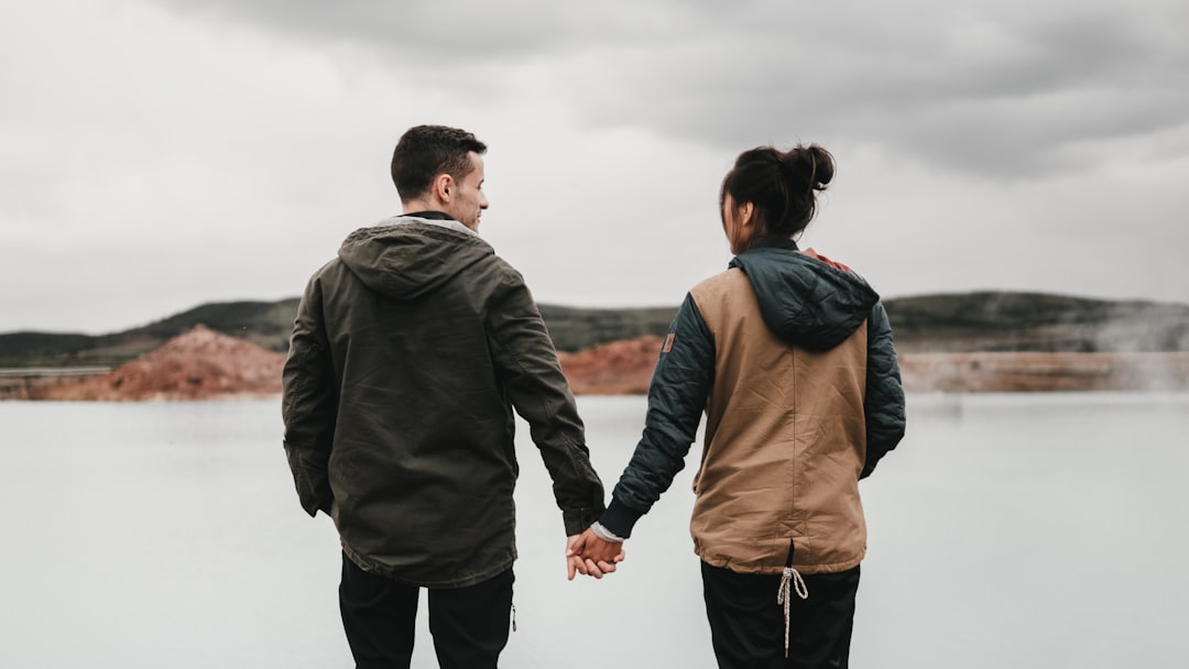 couple walking on hill while holding during daytime